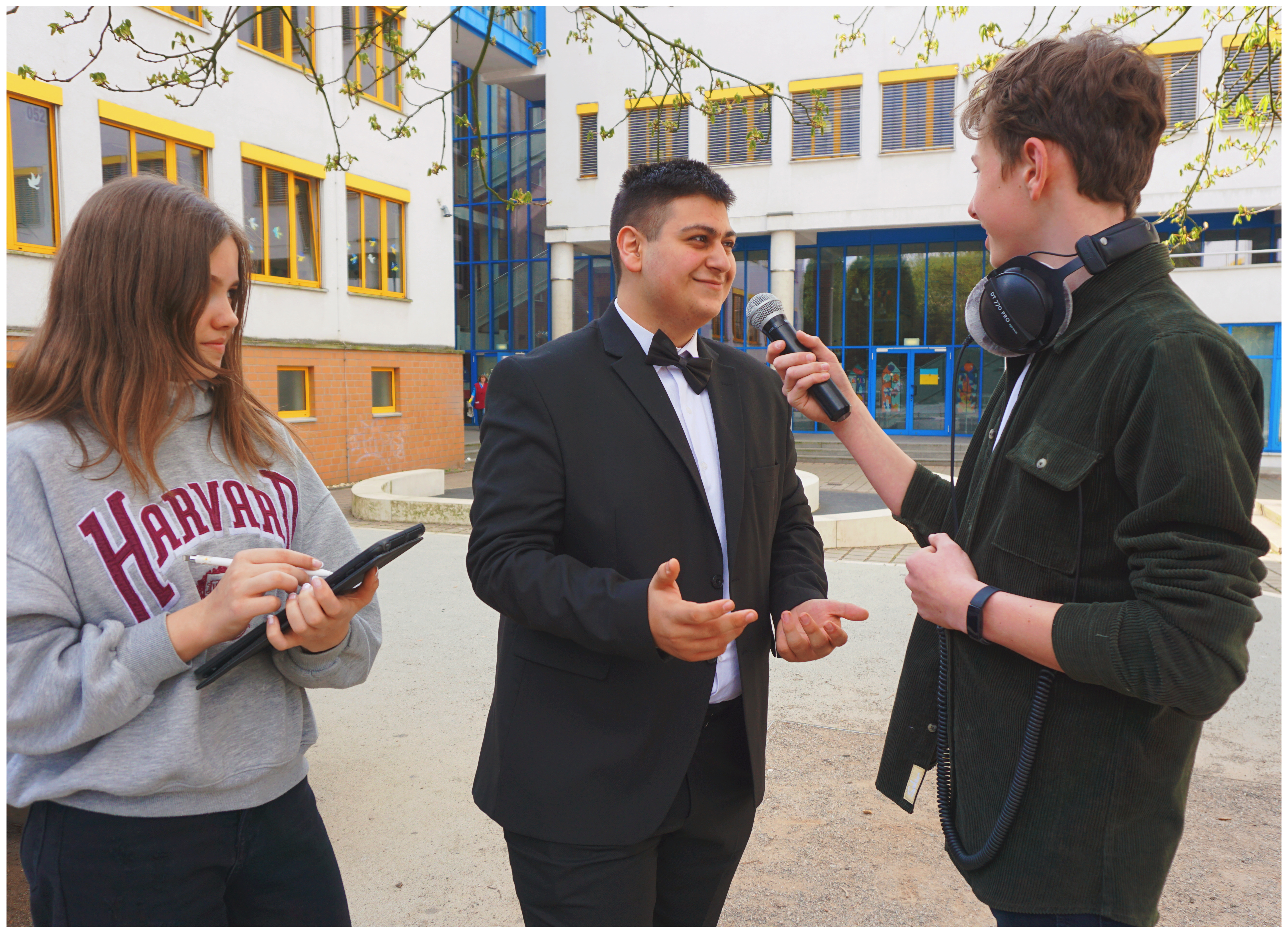 Das Bild zeigt drei Schüler auf dem Schulhof bei einem Interview.