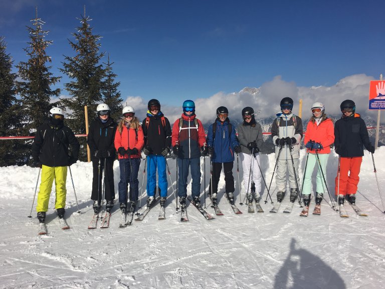 Das Bild zeigt Schüler in Ski-Montur im Schnee bei blauem Himmel.